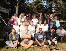 A large group of people poses outdoors for a photo among trees.