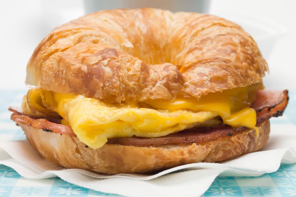 A buttery croissant sandwich filled with ham, scrambled eggs, and melted cheese.