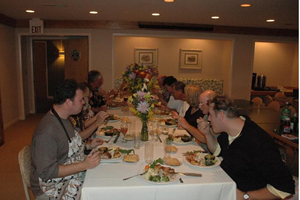 A group of people enjoying a meal together at a long dining table adorned with flowers.