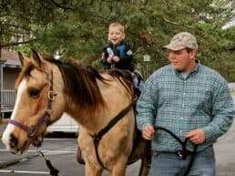A young boy joyfully rides a horse while being led by a man.