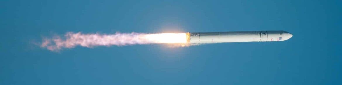 A rocket launches into a blue sky, trailing smoke.