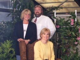 Three people posing together in a garden setting.