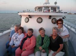 A group of six women seated on the deck of a boat, enjoying a sunset at sea.