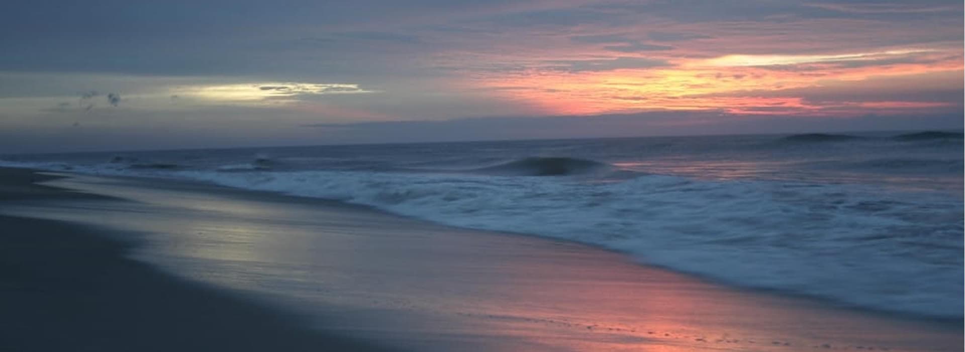 A serene beach at sunset with gentle waves and colorful sky reflections.