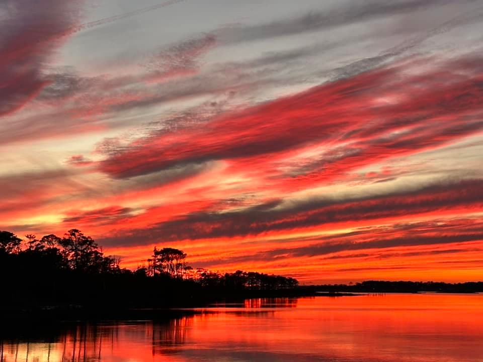 Vibrant sunset reflecting on calm water, framed by silhouetted trees. Vibrant sunset reflecting on calm water, framed by silhouetted trees.