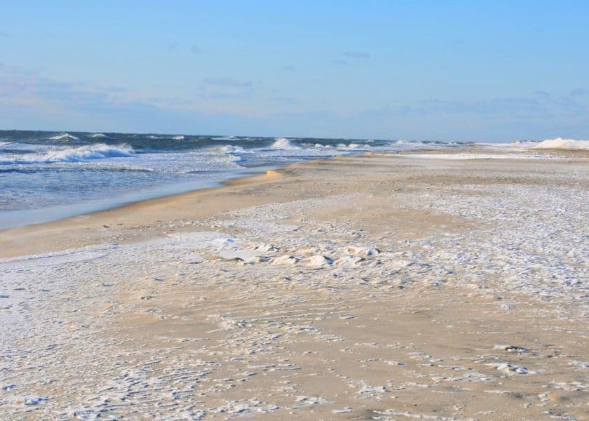 A tranquil beach scene with gentle waves lapping at the sandy shore under a blue sky. A tranquil beach scene with gentle waves lapping at the sandy shore under a blue sky.