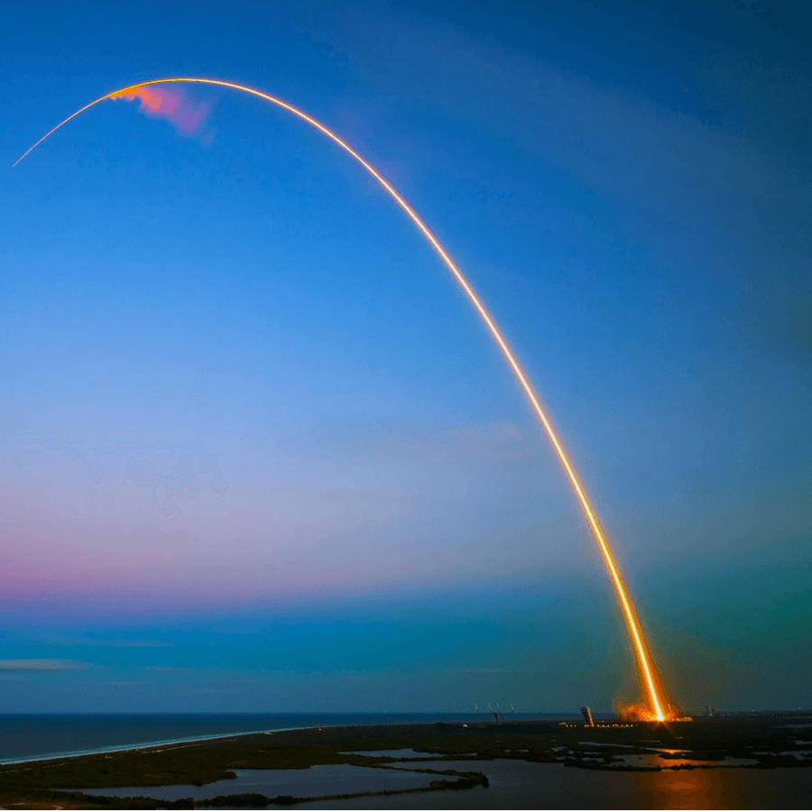 A rocket launches, leaving a bright arc against a twilight sky.