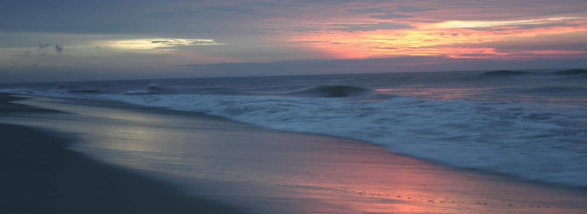 A tranquil beach at sunset with gentle waves reflecting colorful skies.
