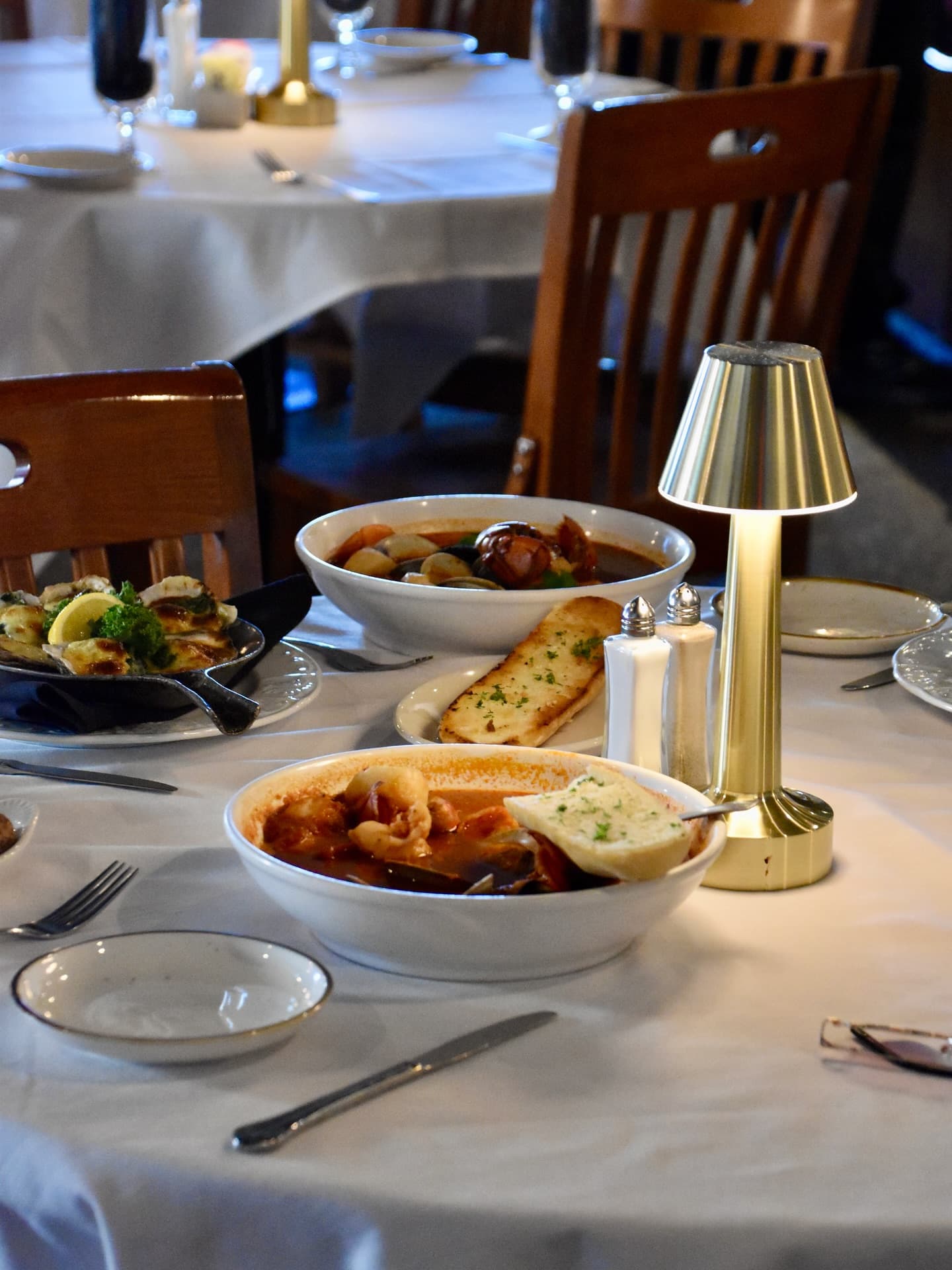 A cozy meal of cioppino and oysters rockefeller is presented at Bill's Prime Seafood and Steaks, complete with table lamp, white tablecloth, and thoughtful place settings. A cozy meal of cioppino and oysters rockefeller is presented at Bill's Prime Seafood and Steaks, complete with table lamp, white tablecloth, and thoughtful place settings.