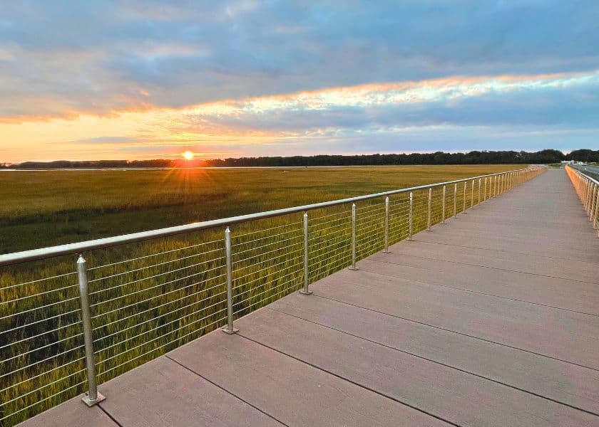A wooden boardwalk on Chincoteague with metal cable railings stretches across marshland toward a low sunset A wooden boardwalk on Chincoteague with metal cable railings stretches across marshland toward a low sunset