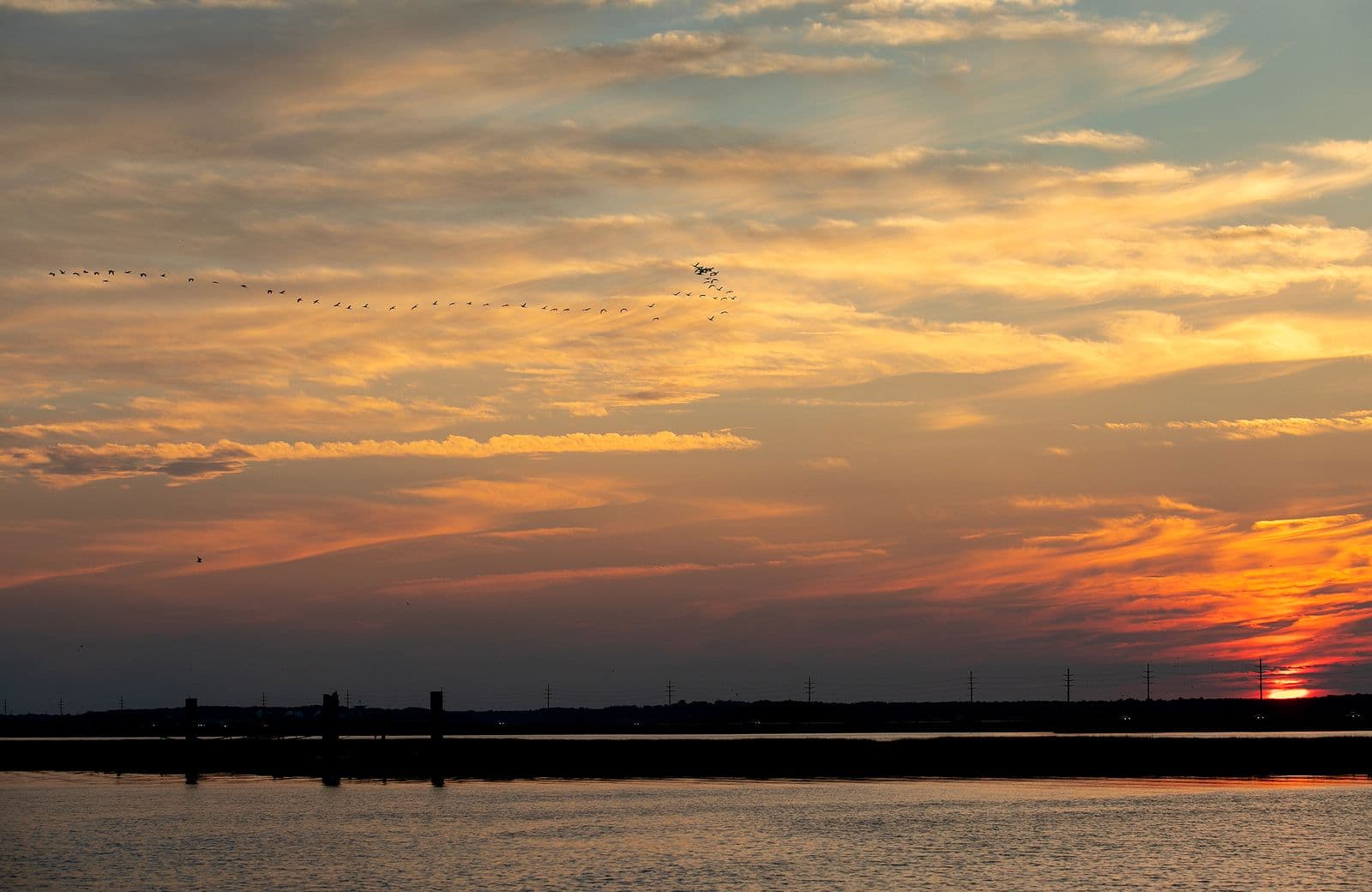 The sun sets over the Chincoteague channel as a flock of waterfowl fly overhead The sun sets over the Chincoteague channel as a flock of waterfowl fly overhead